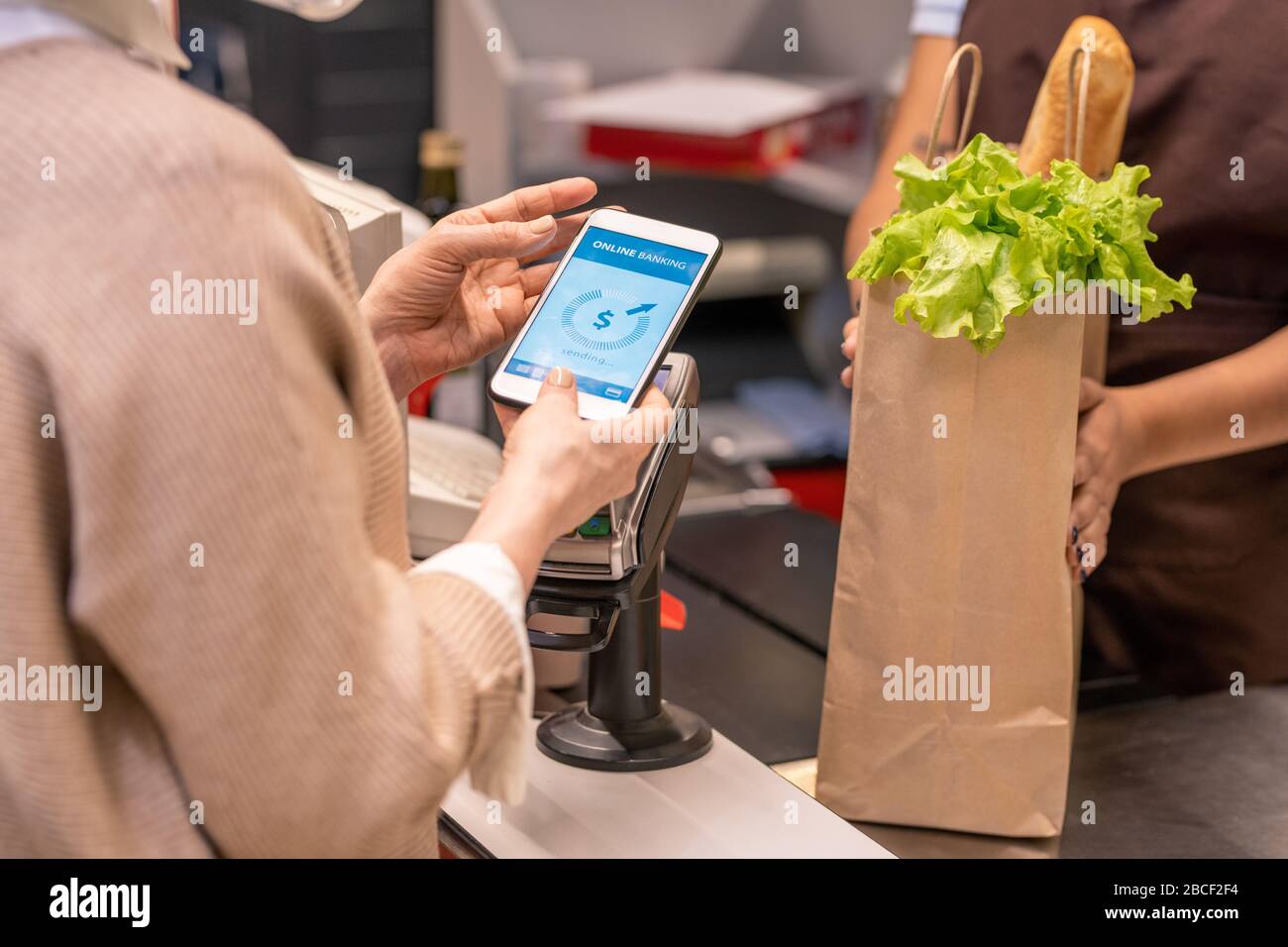 Hände reifer Einkäufer mit Smartphone über Zahlmaschine, die Lebensmittel im Supermarkt per Kasse bezahlen Stockfoto