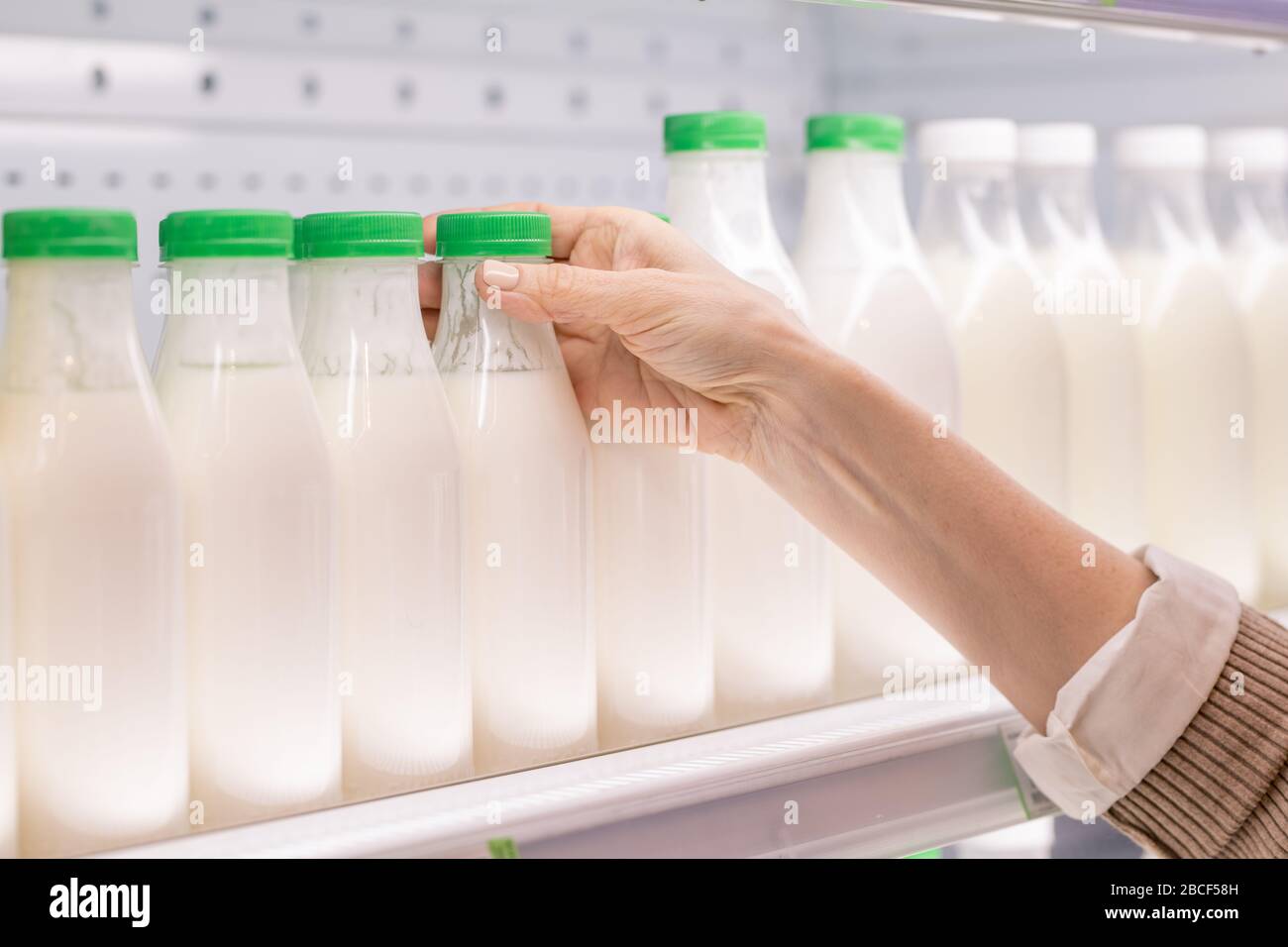 Hand der alten Konsumentin, die im Supermarkt eine Plastikflasche frischen sauren Milchgetränks bei der Auswahl von Lebensmitteln mitnimmt Stockfoto