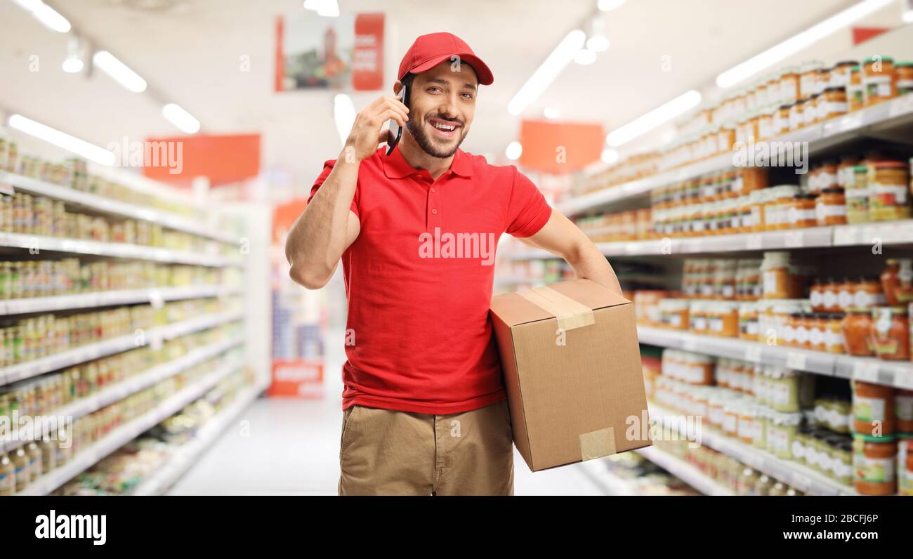 Der Liefermann spricht auf einem Handy und hält ein Paket in einem Supermarkt Stockfoto
