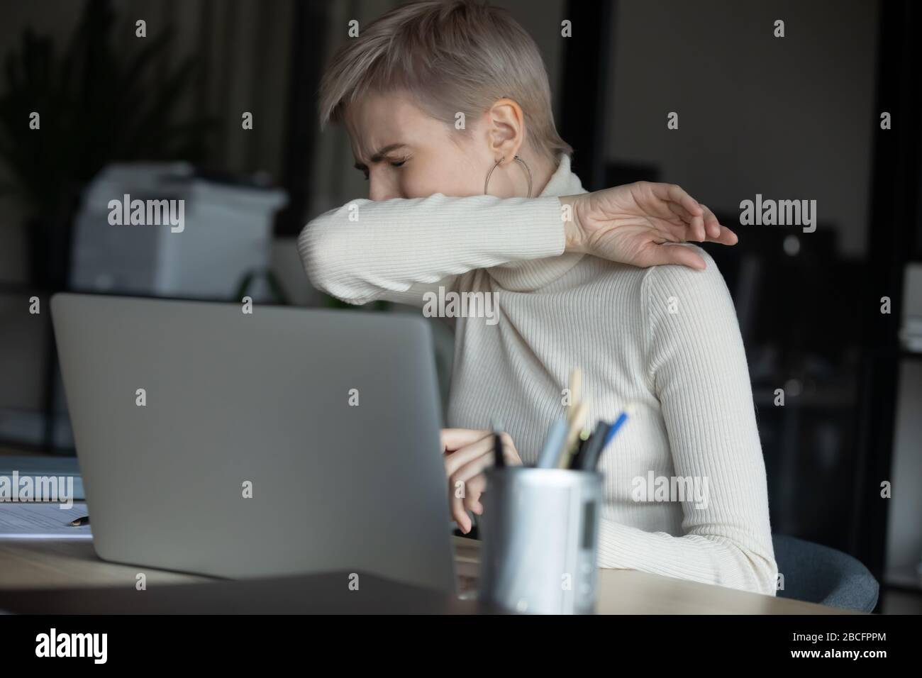 Kranke junge Arbeiterantin hustet Niesen im Ellenbogen. Stockfoto