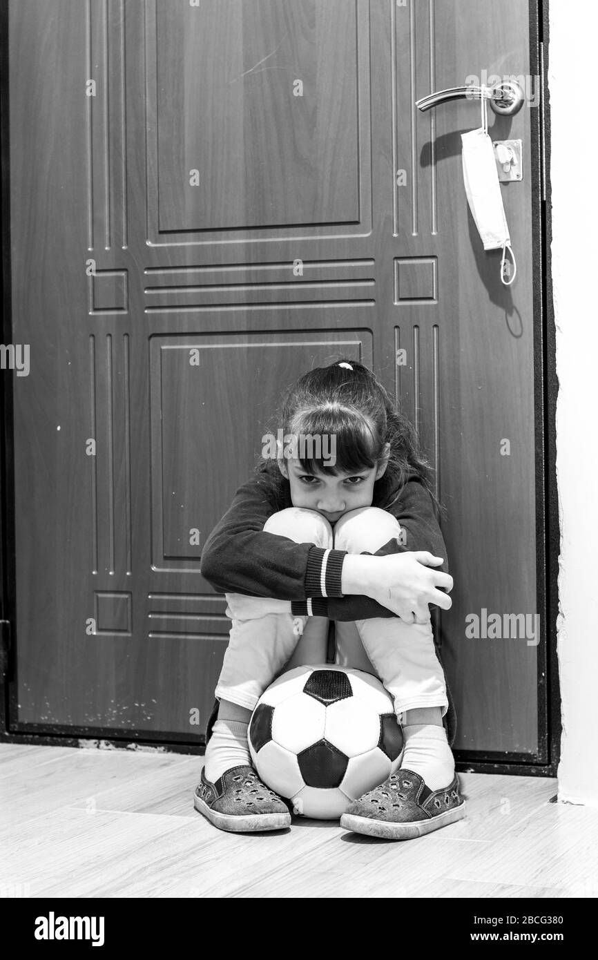 Ein Mädchen sitzt mit einem Ball an der Haustür, darf aber während der Quarantäne nicht nach draußen gehen Stockfoto