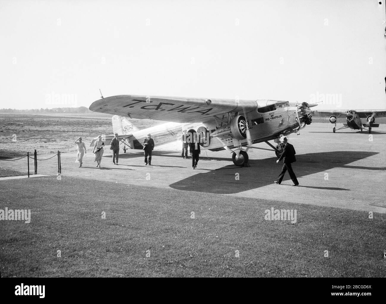 Passagiere gehen auf dem Asphalt, nachdem sie ein Flugzeug der City of Indianapolis T&WA Air Mail, 1934, deplaniert haben. Fotografie von Burton Holmes. Stockfoto