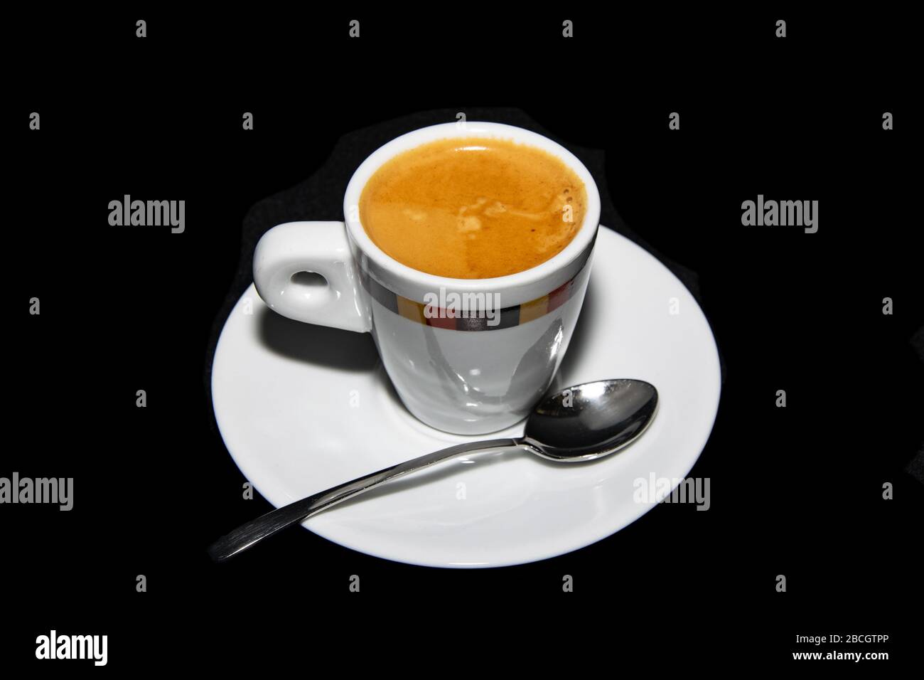 Eine Tasse frisch gemahlener doppelter Espresso-Kaffee neben einem Teller und einem Löffel Stockfoto