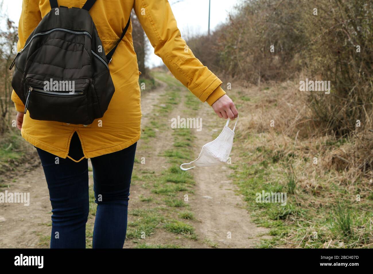 Frau hält die textile hausgemachte Gesichtsmaske, die zum Schutz vor Viren verwendet wird, während sie in der Natur spaziert. Stockfoto