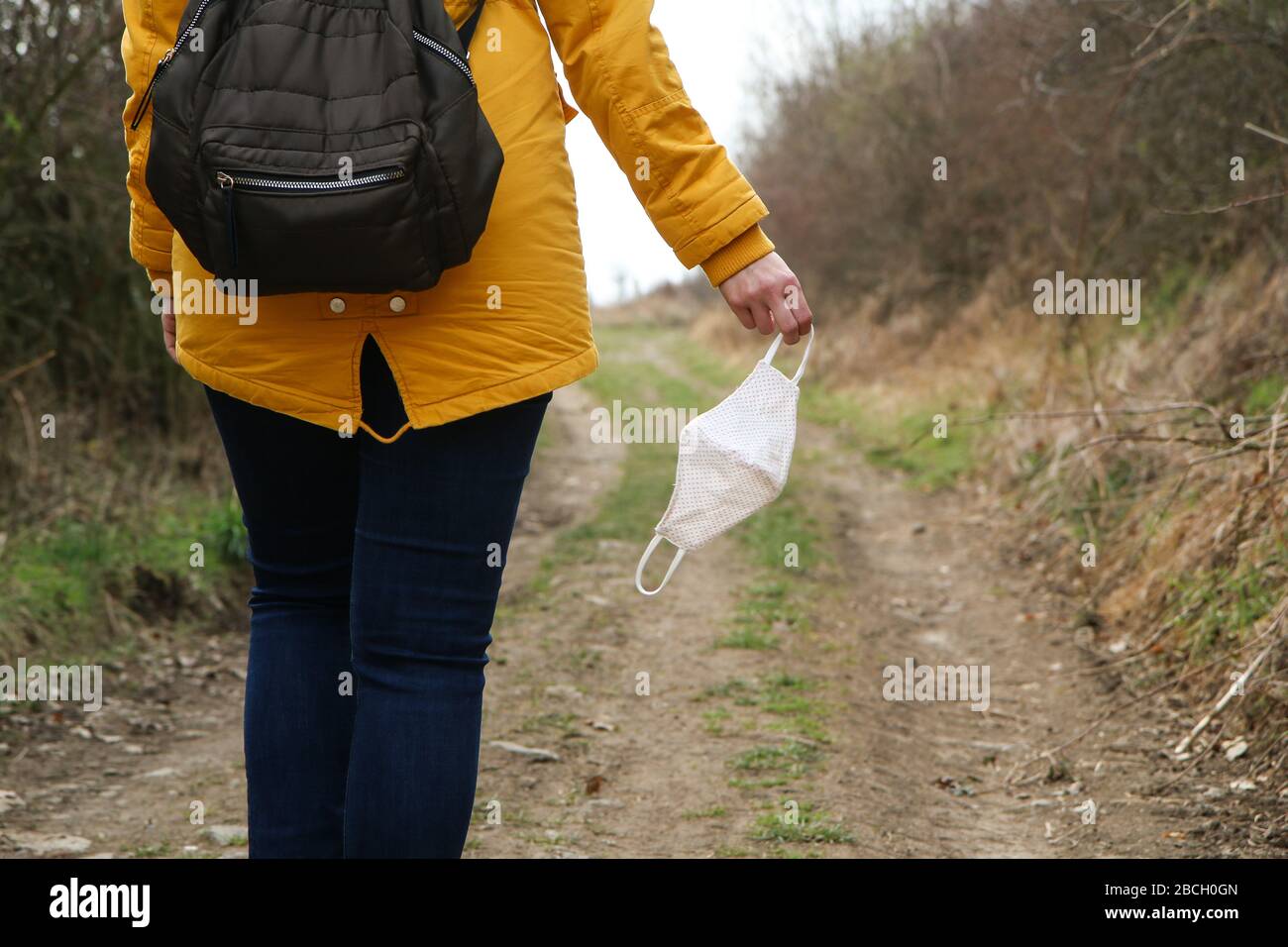 Frau hält die textile hausgemachte Gesichtsmaske, die zum Schutz vor Viren verwendet wird, während sie in der Natur spaziert. Stockfoto