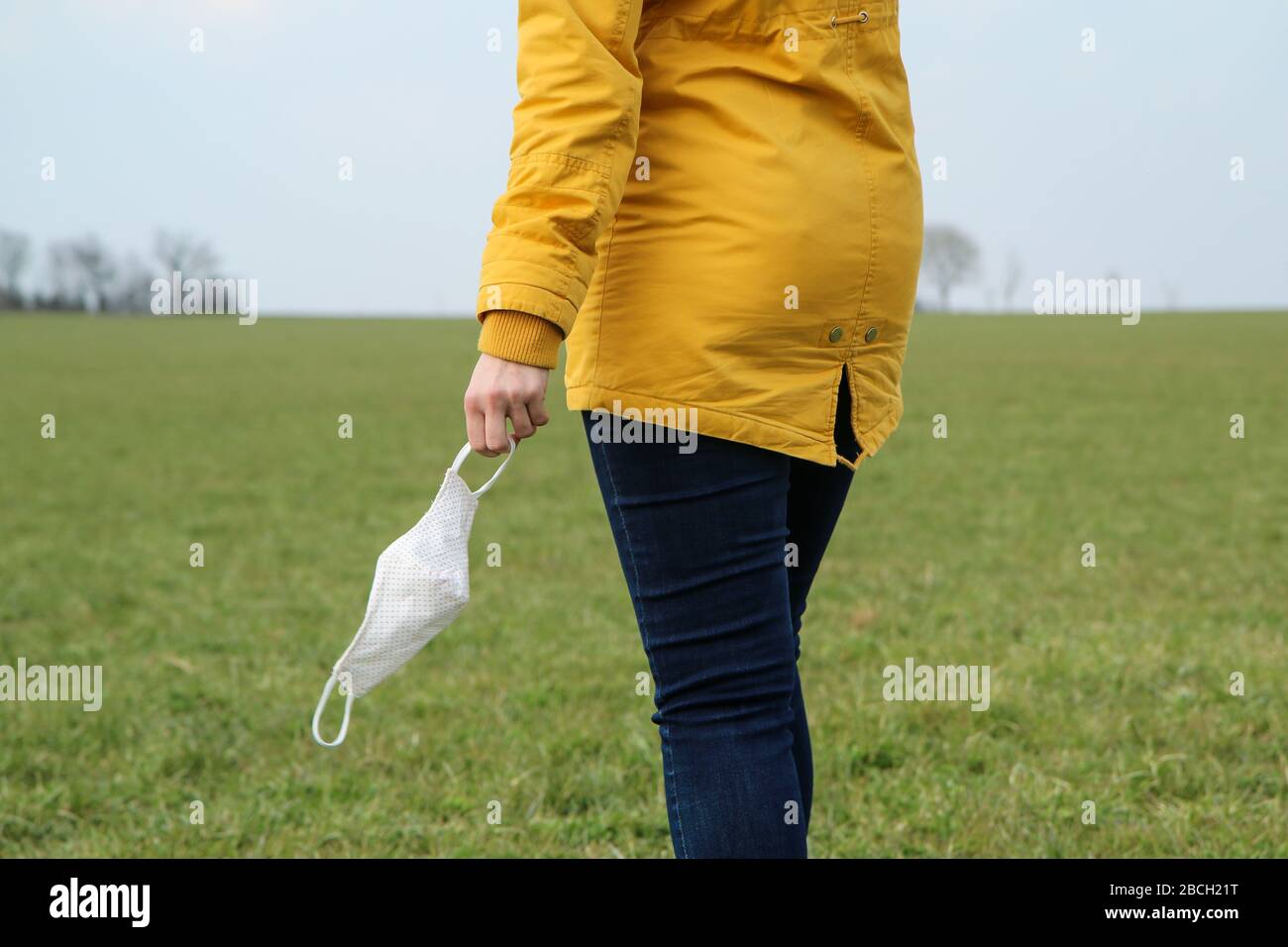 Frau hält die textile hausgemachte Gesichtsmaske, die zum Schutz vor Viren verwendet wird, während sie in der Natur spaziert. Stockfoto