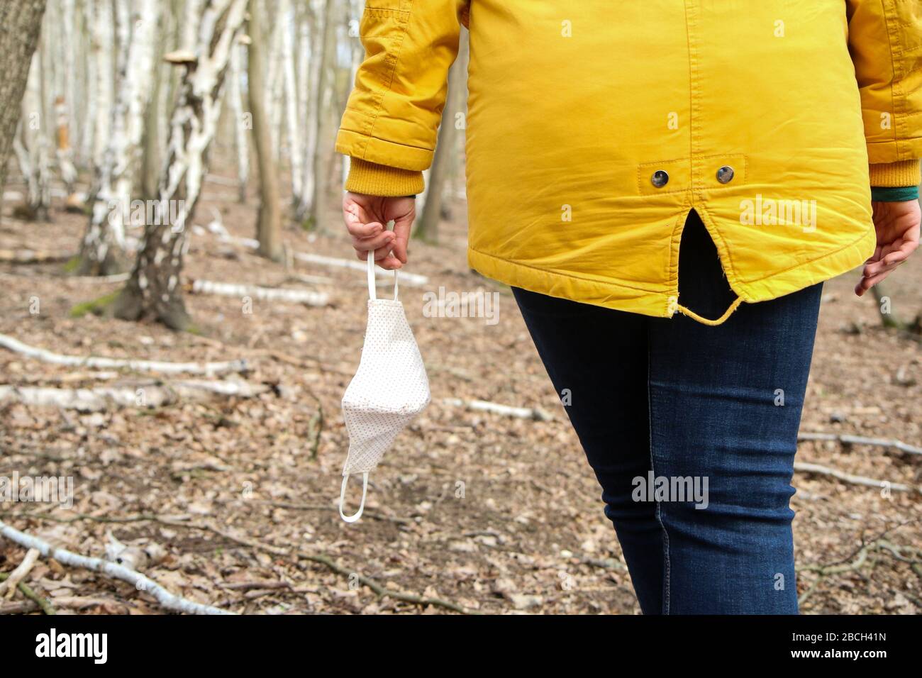 Frau hält die textile hausgemachte Gesichtsmaske, die zum Schutz vor Viren verwendet wird, während sie in der Natur spaziert. Stockfoto