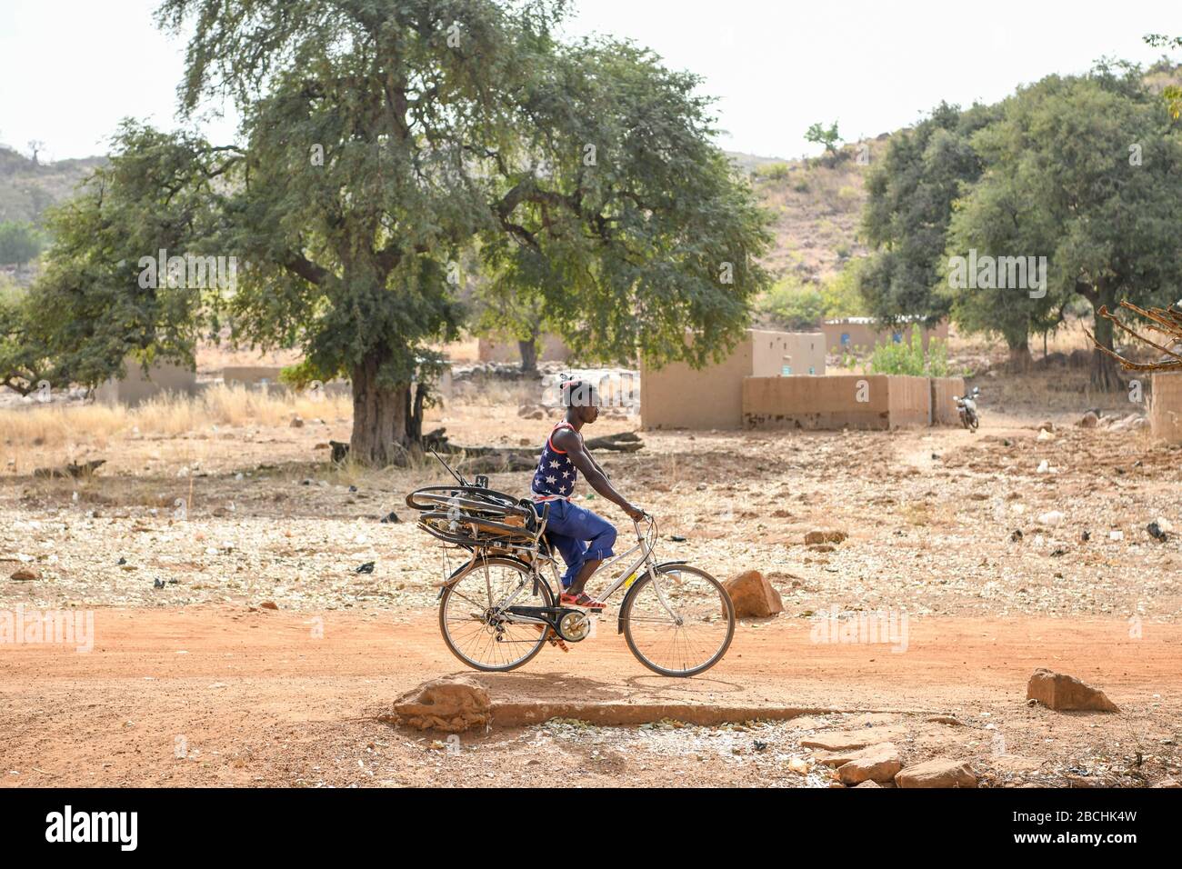 Afrika, Burkina Faso, Region Pô, Tiebele. Ein Mann fährt auf einer unbefestigten Straße mit einem Fahrrad an seinem Fahrrad Stockfoto
