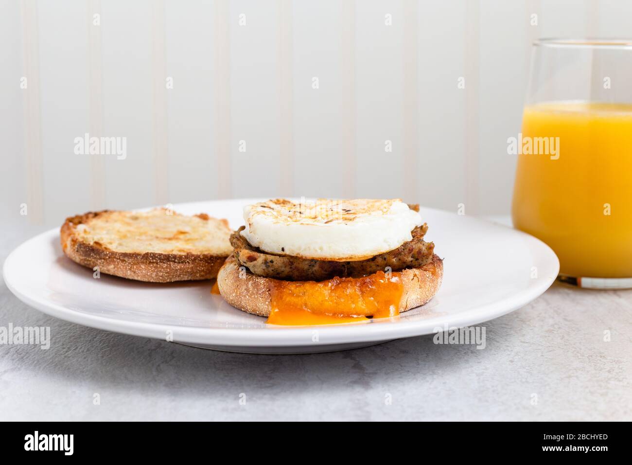 Frühstückssandwich mit Wurst, Ei und Käse und Orangensaft Stockfoto