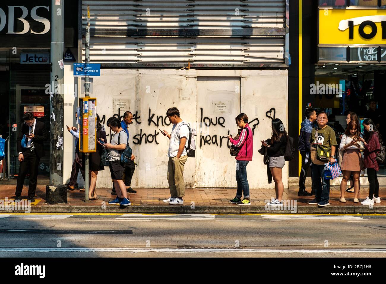 Hongkong - November 2019: Menschen auf der Straße stehen in der Warteschlange und warten auf einen Bus, der auf dem Handy in Hongkong sucht Stockfoto