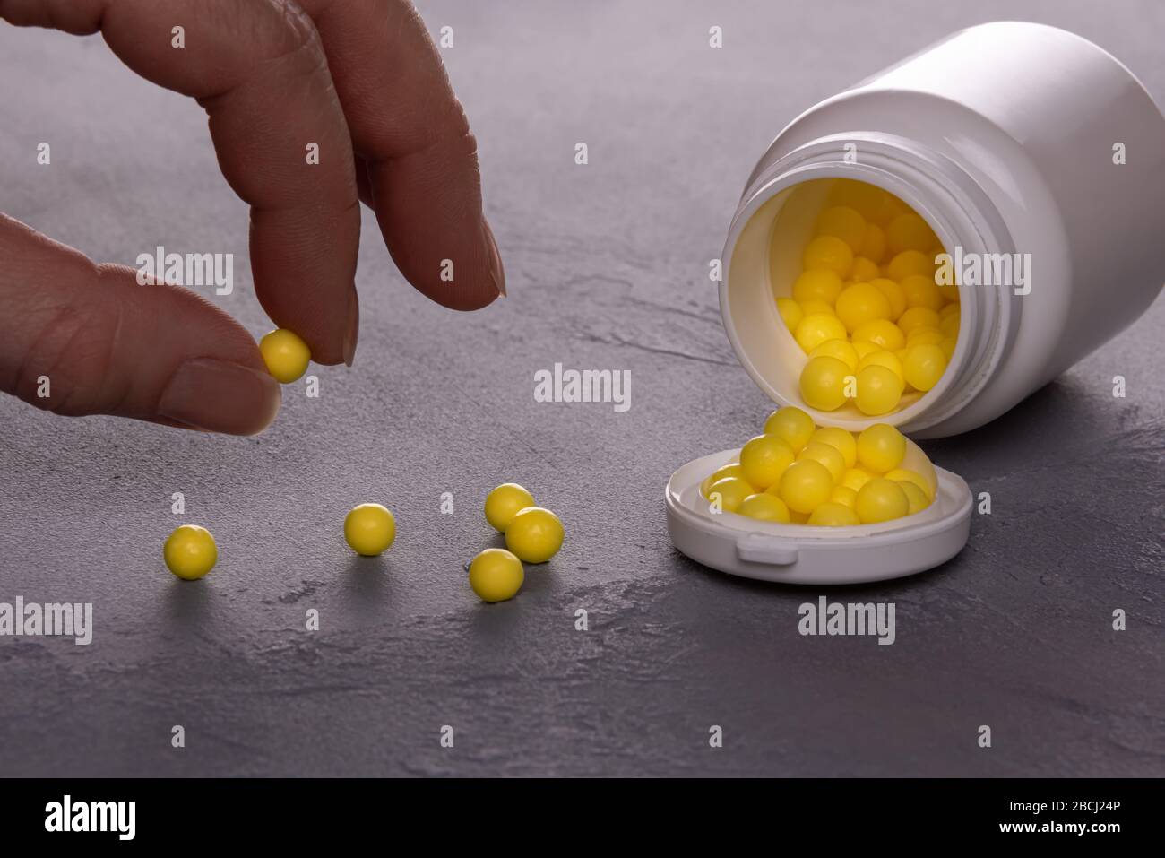 Nahaufnahme der geöffneten weißen Plastikflasche, die seitlich liegt und voll kleiner runder gelber Tabletten von Vitamin C. wenige Pillen sind über die Oberfläche verstreut Stockfoto