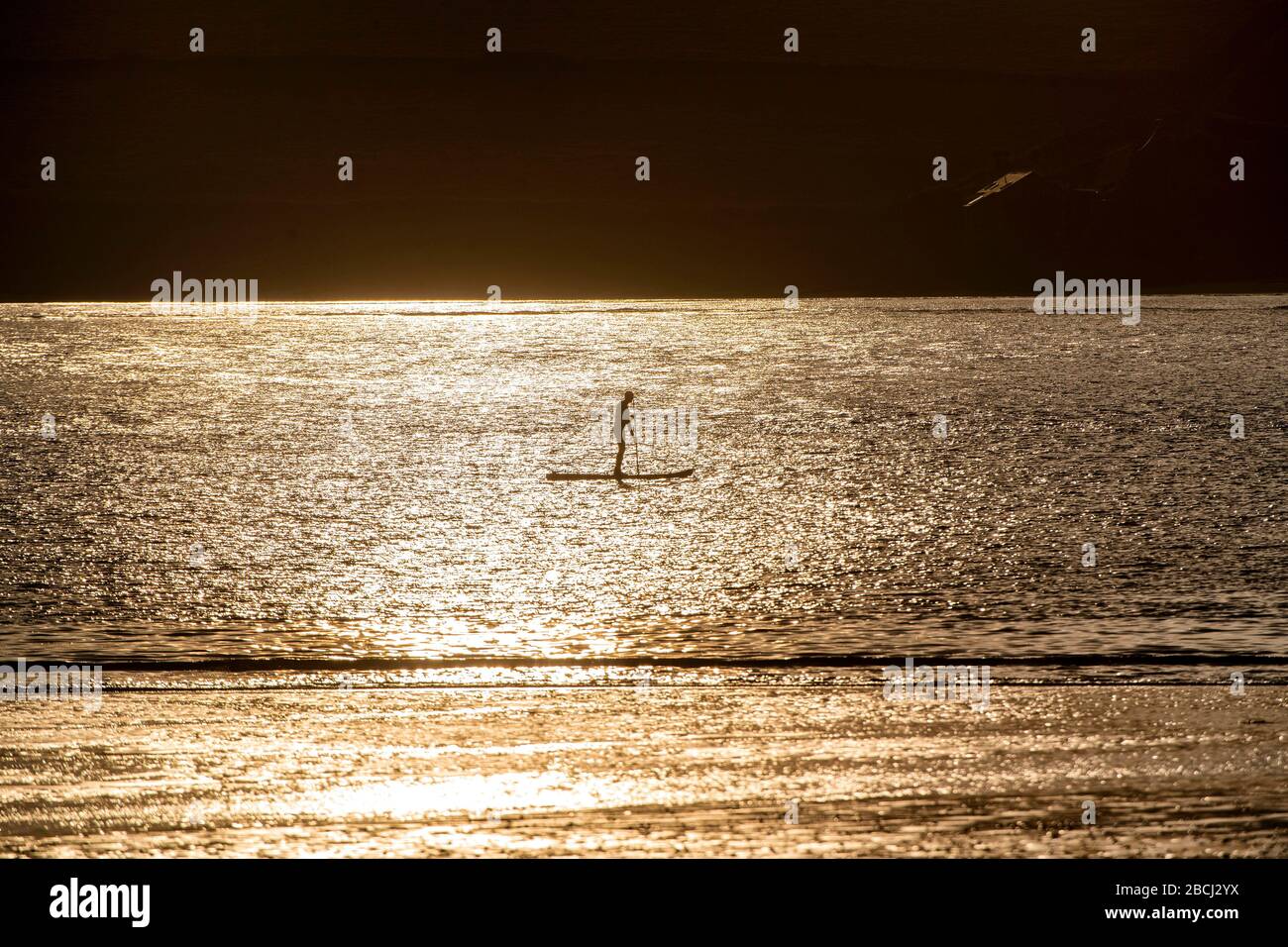 Ein Mann paddelt bei Sonnenuntergang an der Daymer Bay in der Camel Estuary, Cornwall, wenn die Regierungsbeschränkungen im Kampf gegen Coronavirus andauern. Stockfoto