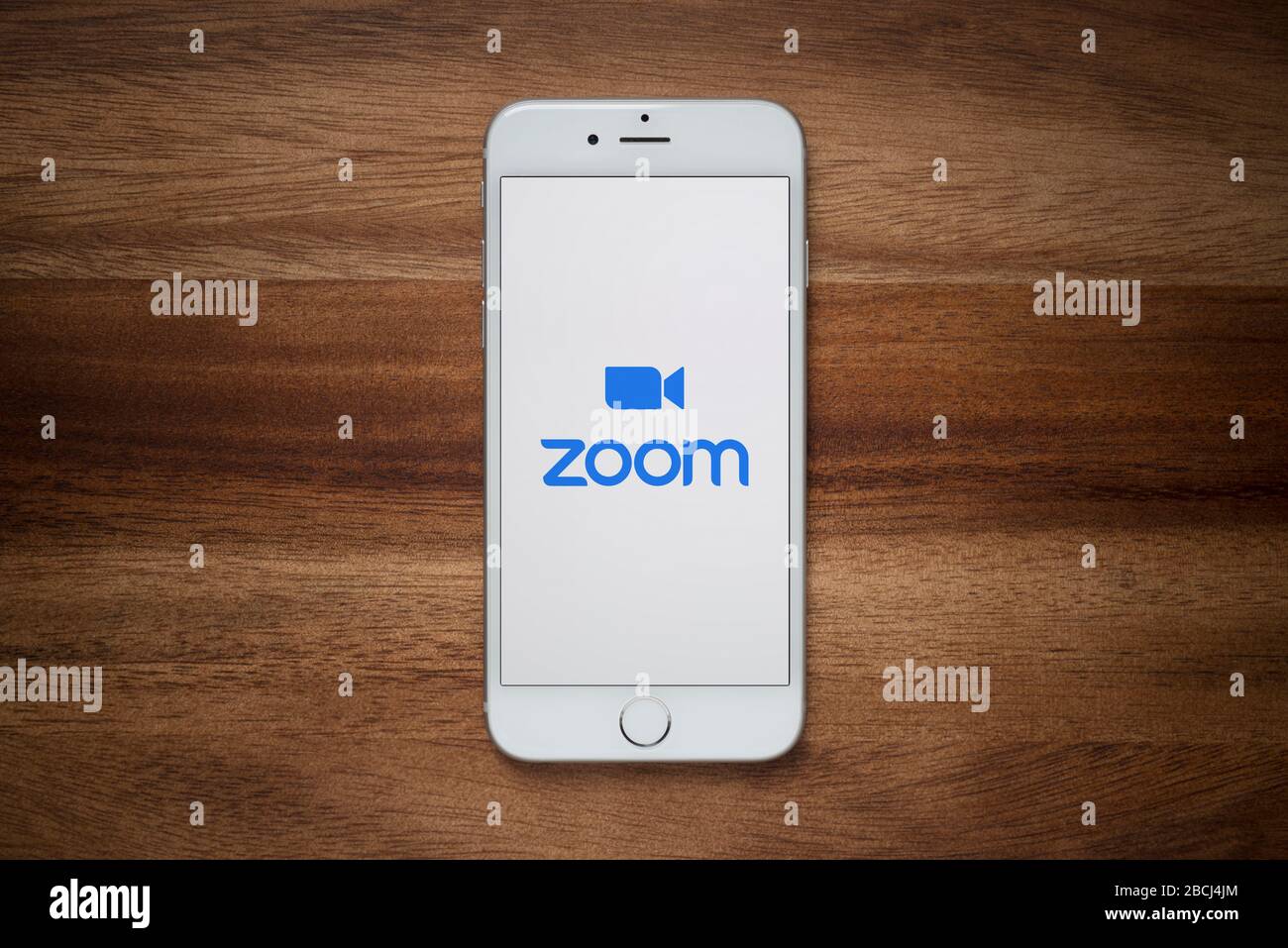 Ein iPhone, auf dem die Website für Videokonferenzen Zoom angezeigt wird, ruht auf einem einfachen Holztisch (nur für redaktionelle Zwecke). Stockfoto
