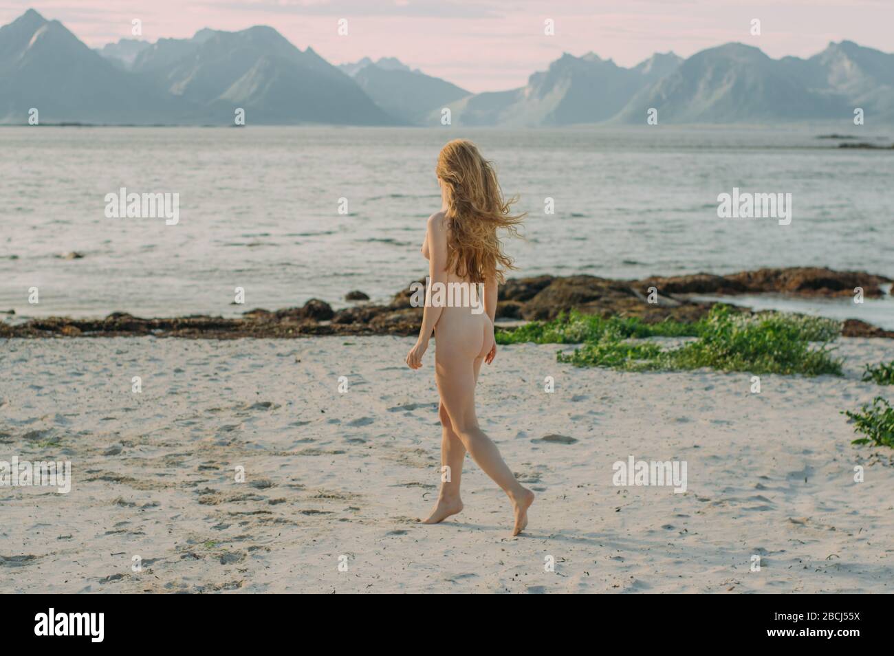 Junges, nacktes blondes Mädchen, das tagsüber am weißen Strand in der Nähe des Meeres, Lofoten Islands, Norwegen, spazieren geht Stockfoto