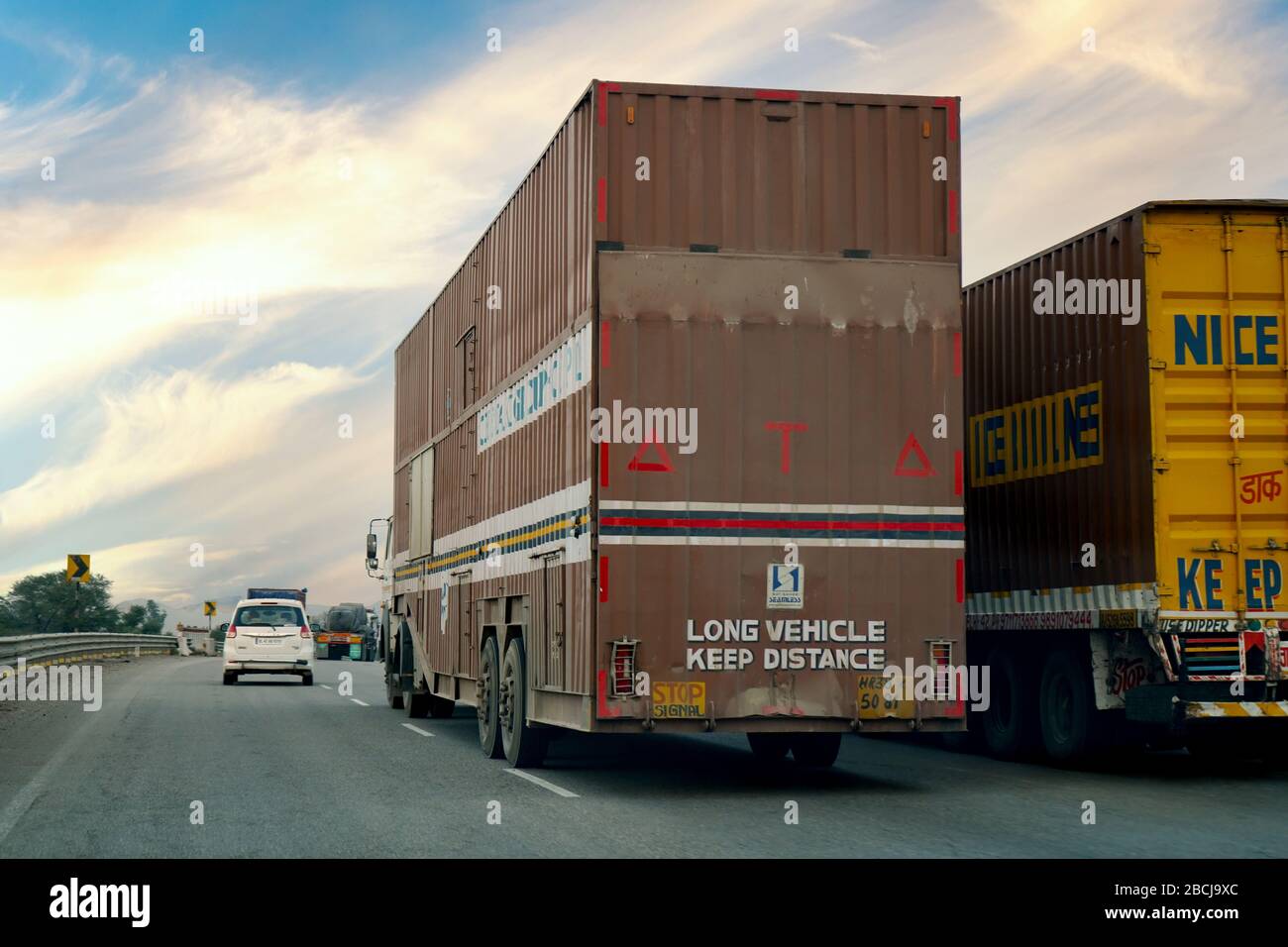 Zwei überdachte Lastwagen mit einem Auto in der Ferne auf einer langen indischen Autobahn Stockfoto