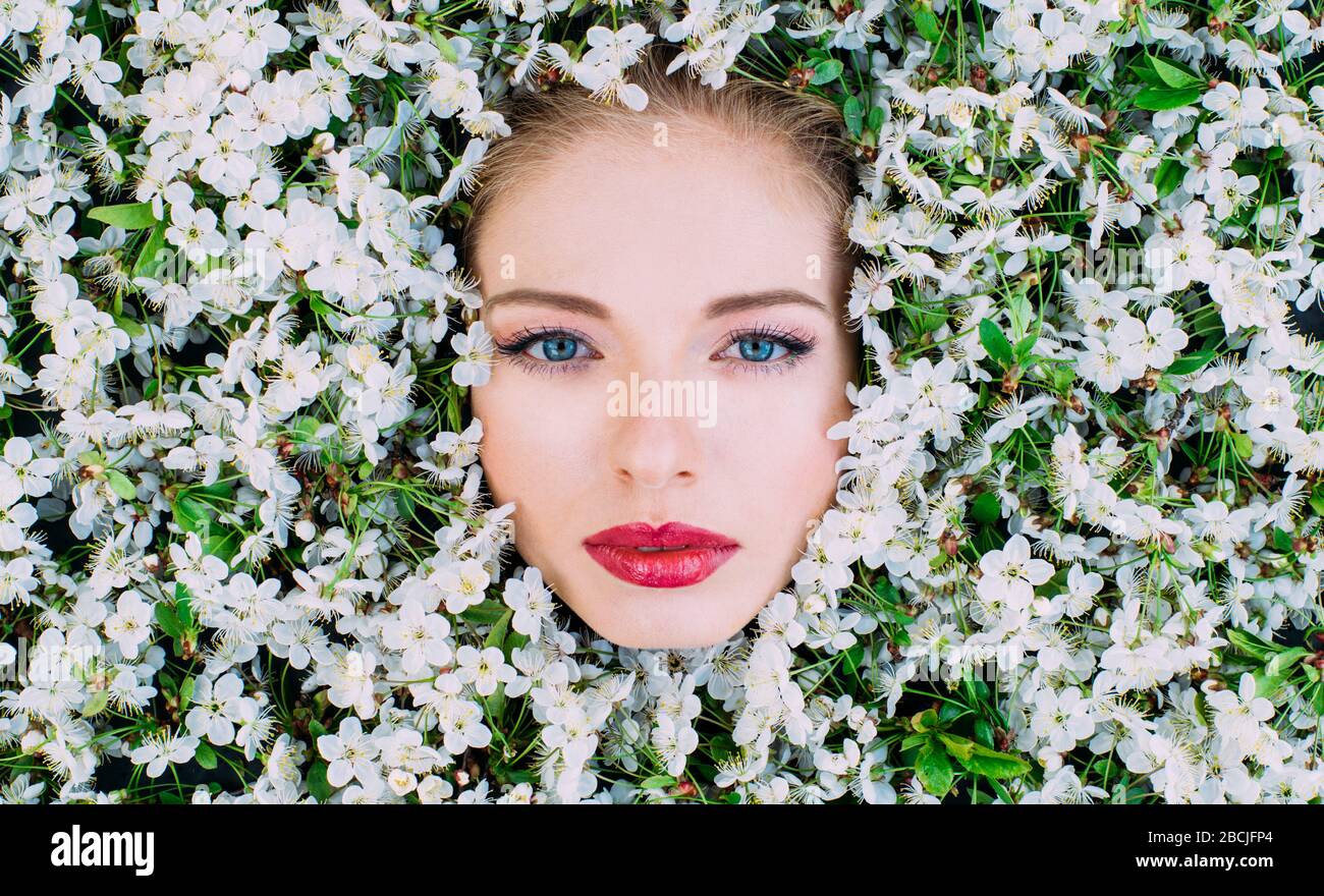 Porträt einer schönen jungen Frau mit roten Lippen und blauen Augen unter den Kirschblüten Stockfoto