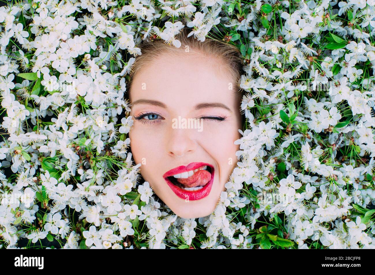 Porträt einer schönen jungen Frau mit roten Lippen und Zunge unter den Kirschblüten Stockfoto