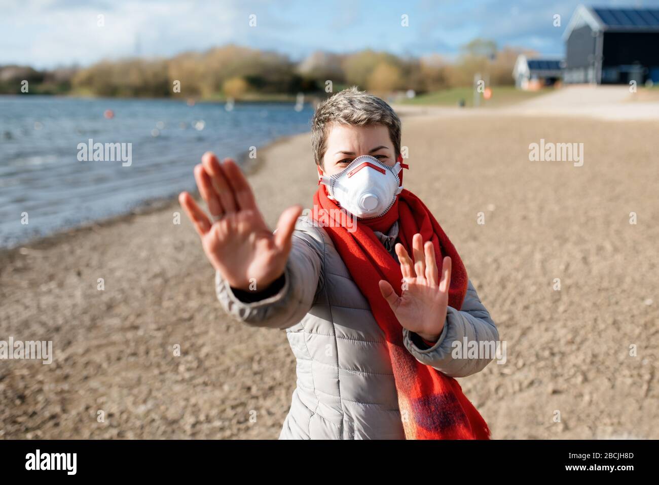 Frau, die eine weiße und rote Gesichtsmaske, eine graue Jacke und einen roten Schal trägt, der IM Freien HALT für Coronavirus zeigt. Stockfoto