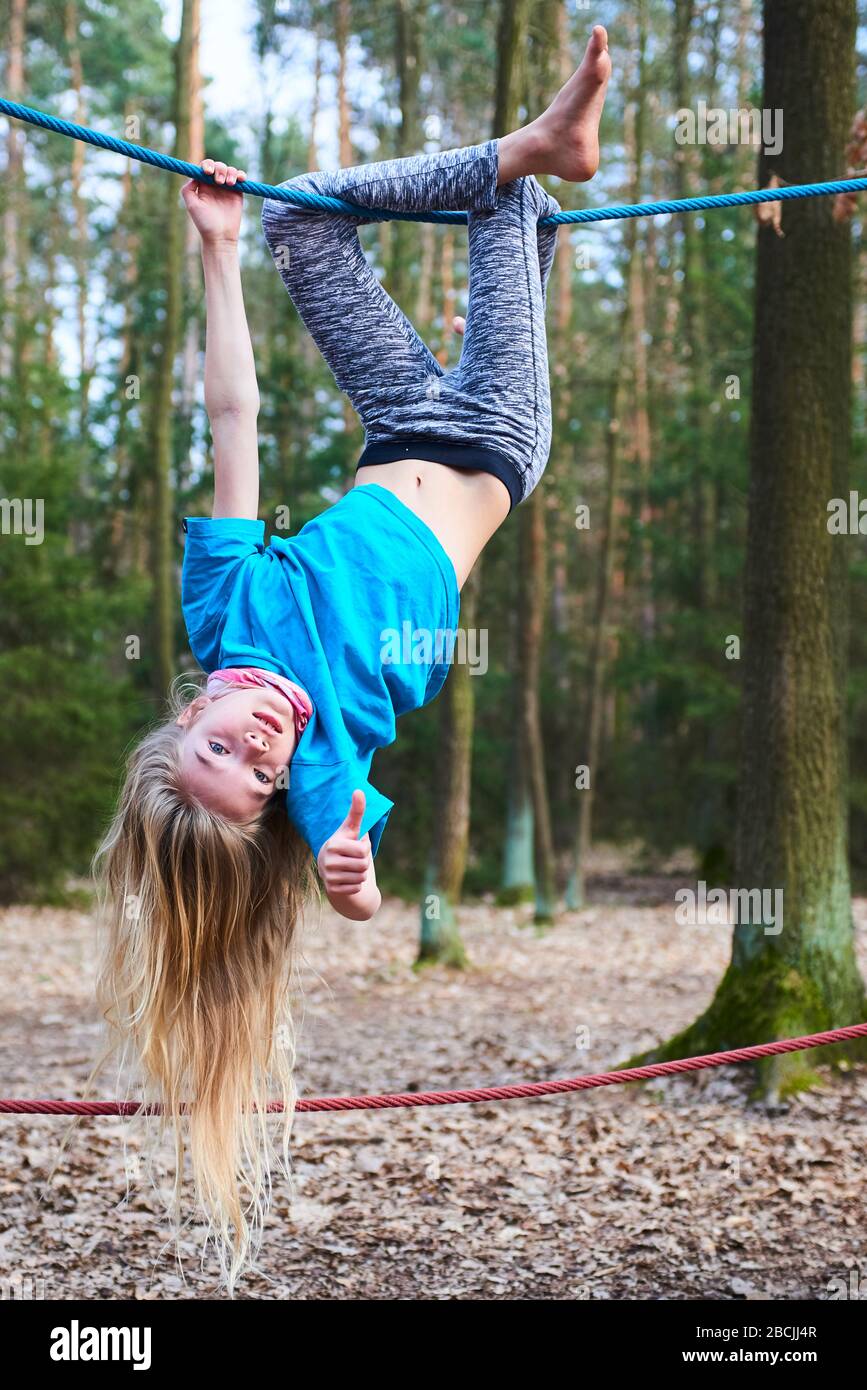 Kleines Mädchen, das auf dem Seil auf dem Spielplatz im Park umgedreht hängt Stockfoto