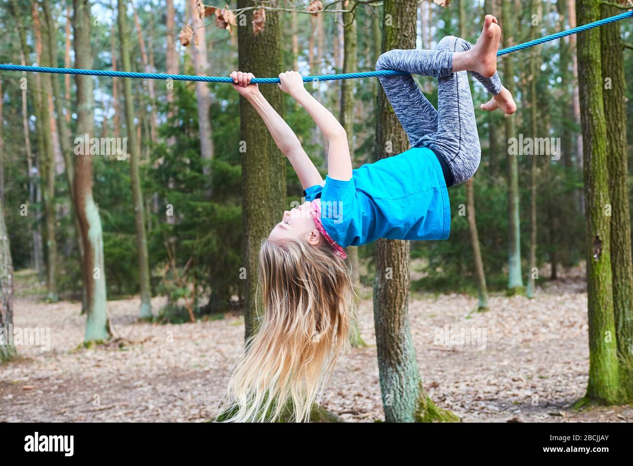 Kleines Mädchen, das auf dem Seil auf dem Spielplatz im Park umgedreht hängt Stockfoto