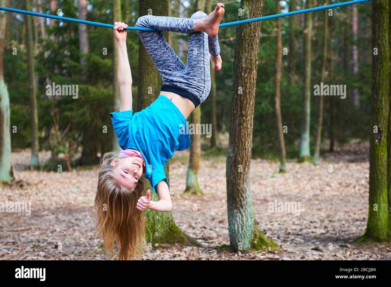 Kleines Mädchen, das auf dem Seil auf dem Spielplatz im Park umgedreht hängt Stockfoto