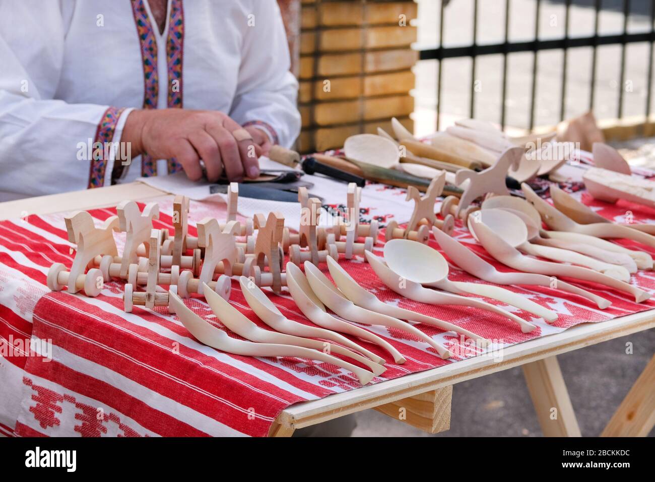 Der Verkäufer legte die handgefertigten Holzhandwerke auf dem Tischtuch mit nationalen Mustern aus. Konzept des nationalen Handwerks. Stockfoto