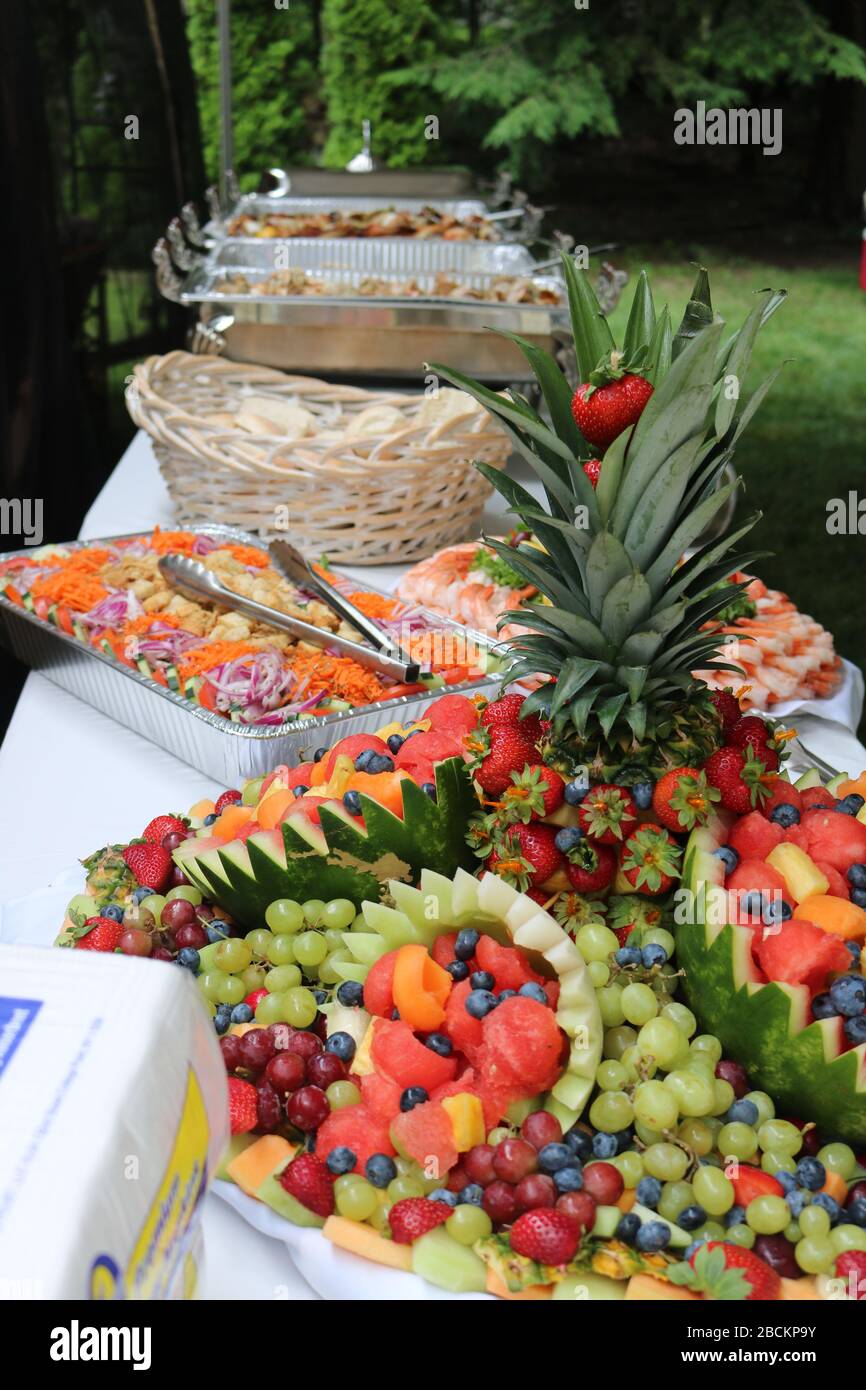 Schöner Banketttisch mit Obstsalat, Salat, Garnelenplatte und Brotkorb. Im Hintergrund sind Scheufchen zu sehen. Schönes Essen. Stockfoto