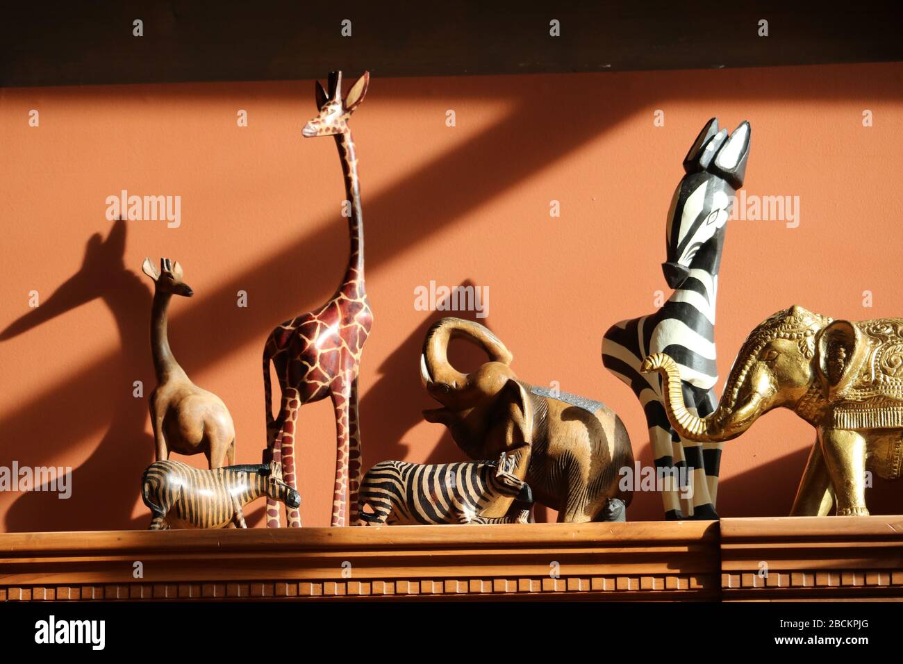 Geschnitzte afrikanische Tiere mit Seitenbeleuchtung, darunter Giraffen, Elefanten und Zebras. Stockfoto
