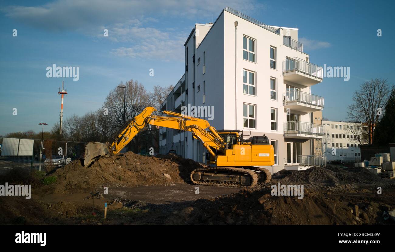 Ein gelber Ausgräber/Bagger, der die Erde vor einem weißen Neubau bewegt Stockfoto