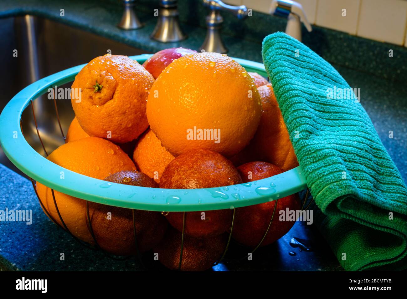 Frisch gereinigter Korb mit Zitrusfrüchten ruht in einem Korb auf dem Küchentisch neben dem Edelstahlwaschbecken in einer Küche. Wassertropfen haften am Stockfoto