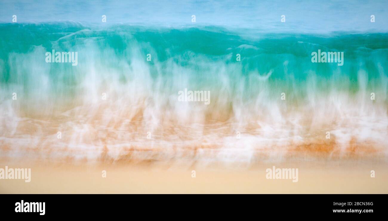 Abstraktes Bild einer abstürzenden Welle am Strand. Kräftige Farben, Aqua, weißer und goldener Sand. Stockfoto
