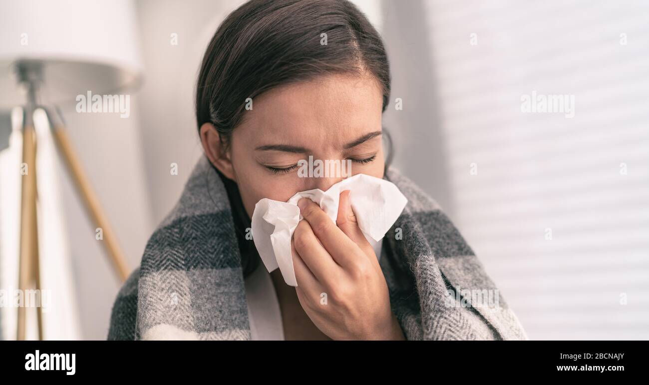 Husten Sie im Gewebe, das Nase und Mund bedeckt, wenn Sie gemäß den COVID-19-Hygienerichtlinien für die Vorbeugung von Coronavirus-Ausbreitung husten. Asian Woman krank mit Grippe zu Hause. Stockfoto