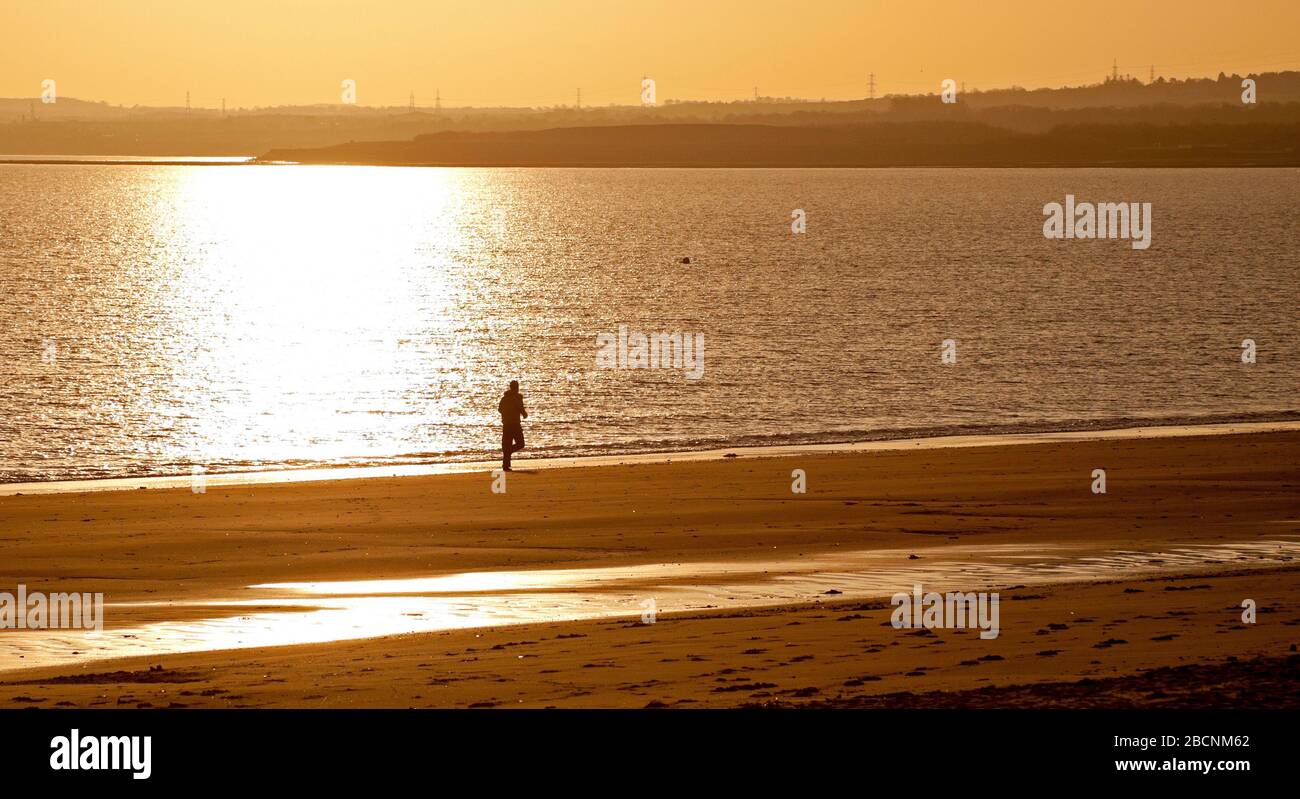 Portobello, Edinburgh, Schottland, Großbritannien. April 2020. Sonnenaufgang am Portobello Beach, mit verschiedenen Leuten, die am Strand laufen, schwimmen, gehen und in der Kontemplation sitzen. Mit leeren Bänken und im Hintergrund ein Foto von der Fotoanzeige "Into the Blue" vom Wissenschaftsfestival 2020, das nie stattfand und der Aqua 1 Seemannsfahrt zugeschrieben wird, Es fotografiert eine Kreuzform aus Muscheln aus dem Meer, die auf dieser zweiten Woche des Covid-19 Coronavirus Sperrens in Großbritannien ergreifend wirkt. Stockfoto