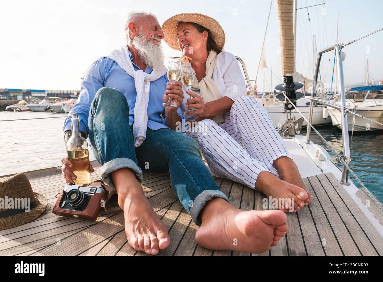 Senioren-Paar jubelt in den Sommerferien mit Champagner auf dem segelboot - reife Leute, die Spaß haben, zusammen zu trinken und zu lachen - fröhliches älteres li Stockfoto