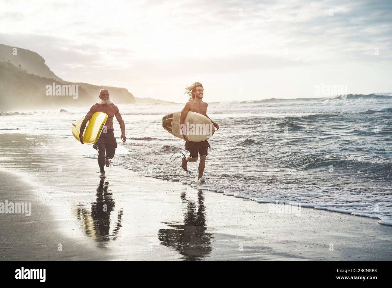 Mehrgenerationige Freunde, die am tropischen Strand surfen - Familienmitglieder haben Spaß am Extremsport - fröhliches älteres und gesundes Lifestyle-Konzept Stockfoto