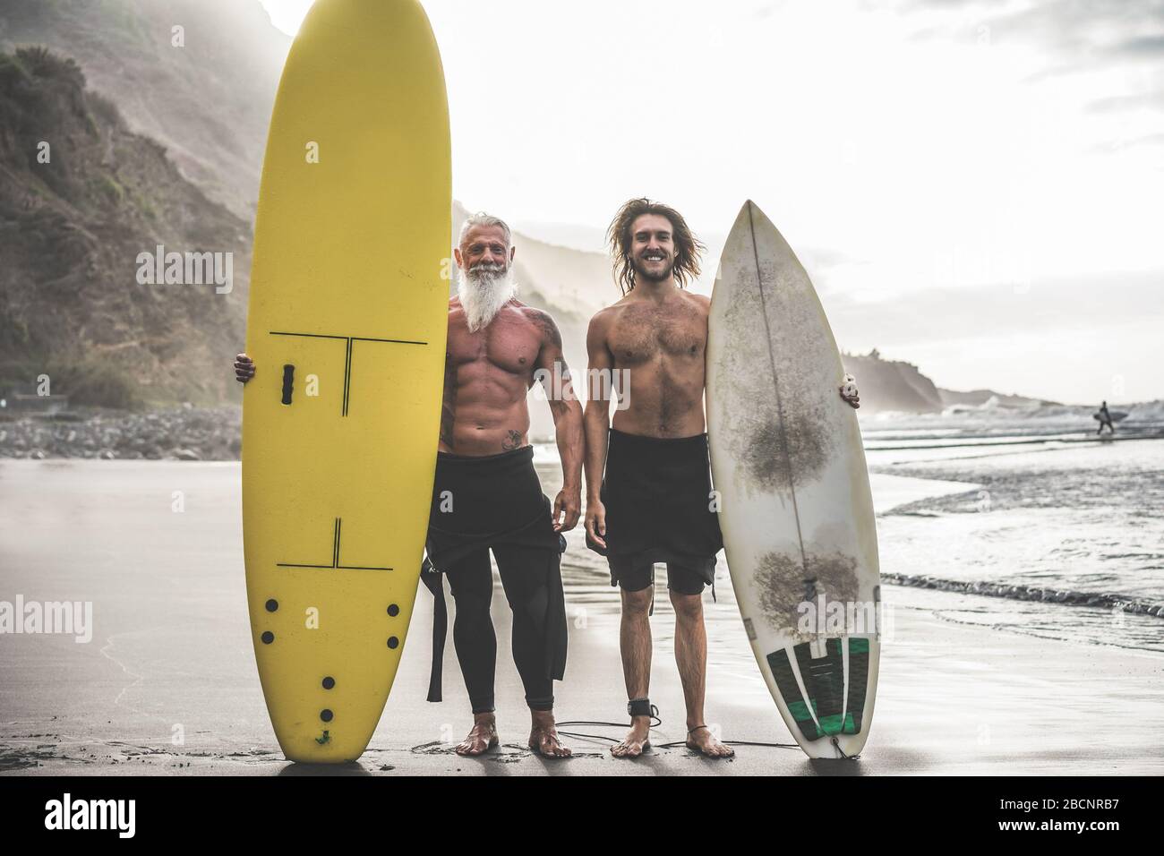 Mehrgenerationige Freunde, die am tropischen Strand surfen - Familienmitglieder haben Spaß am Extremsport - fröhliches älteres und gesundes Lifestyle-Konzept Stockfoto