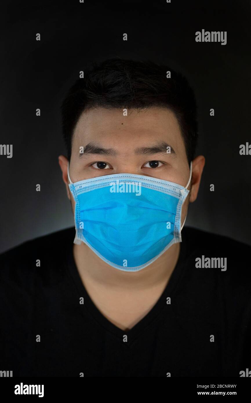 Asiatische Männer tragen eine chirurgisch blaue Maske im schwarzen Hintergrund. Vor Viren, Niesen und Husten schützen Stockfoto