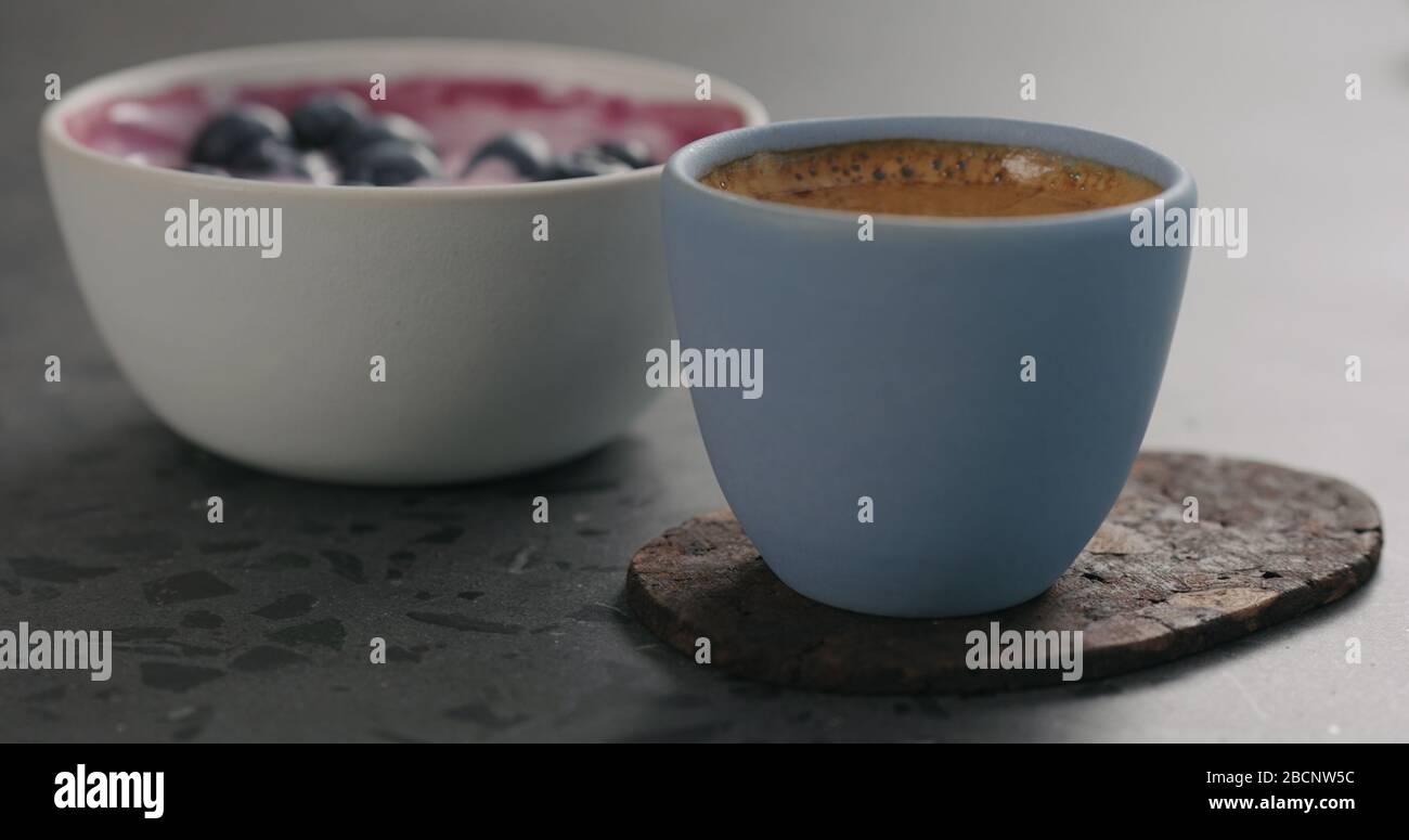 Man Hand setzen blaue Tasse mit frischem Espresso und Heidelbeere Joghurt auf Betonoberfläche Stockfoto