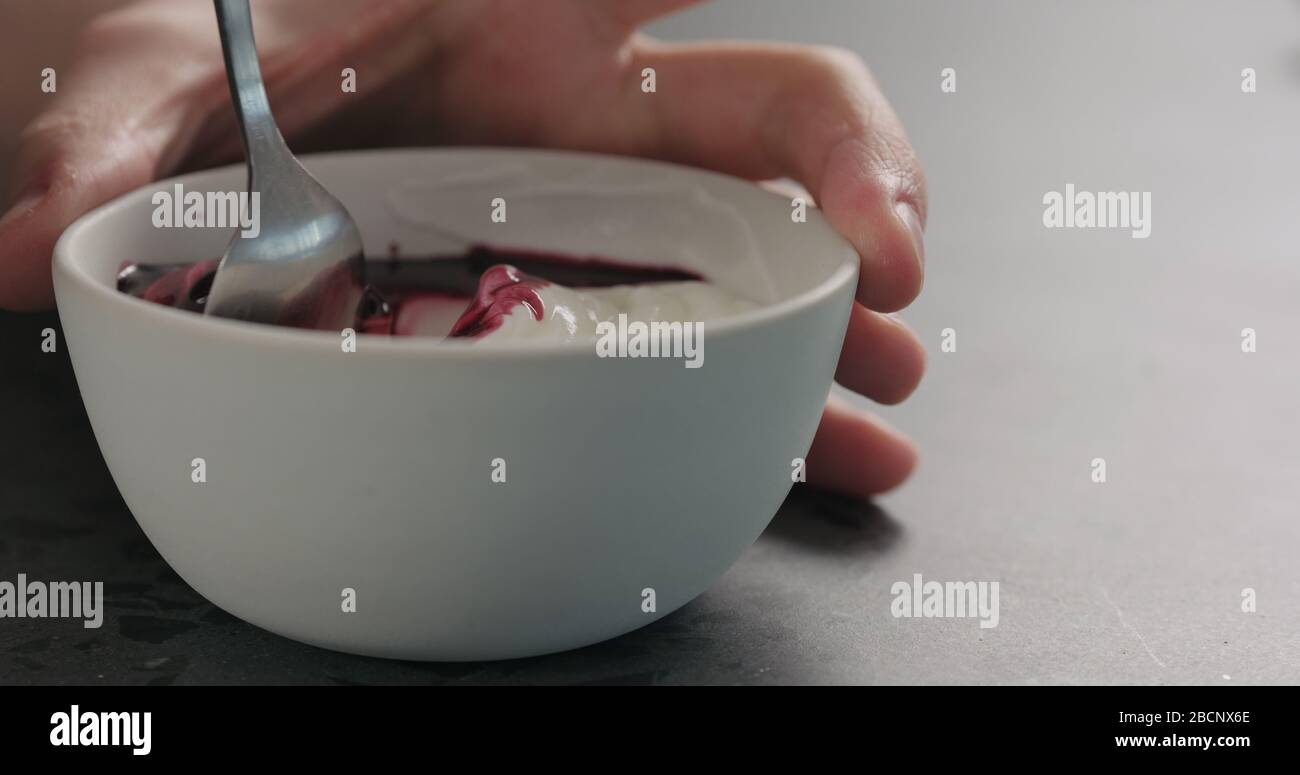 Man Hand mischen Heidelbeersaft mit weißem Joghurt in weiß Schüssel auf Betonoberfläche Stockfoto