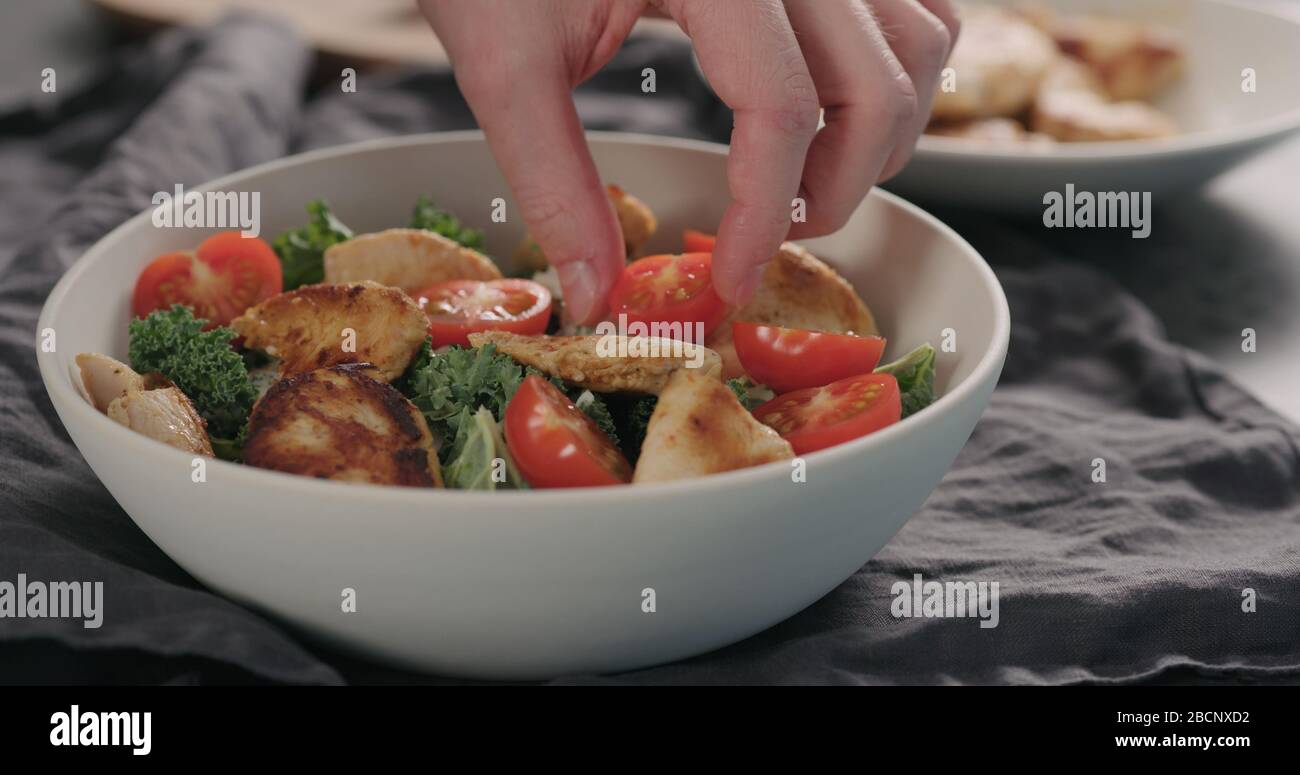 Mann Hände caesar Salat mit Grünkohl und truthahn in einer weißen Schüssel, fügen Sie Tomaten Stockfoto