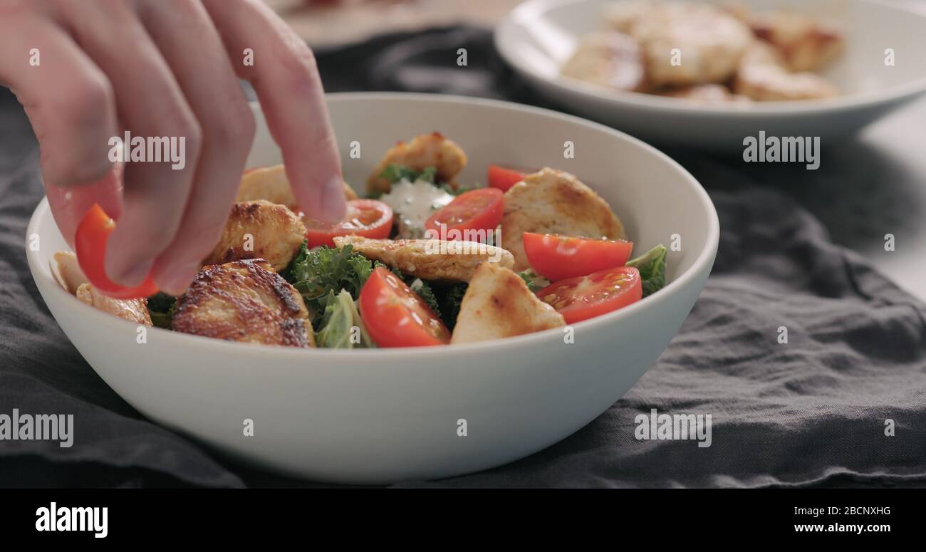 Mann Hände caesar Salat mit Grünkohl und truthahn in einer weißen Schüssel, fügen Sie Tomaten Stockfoto