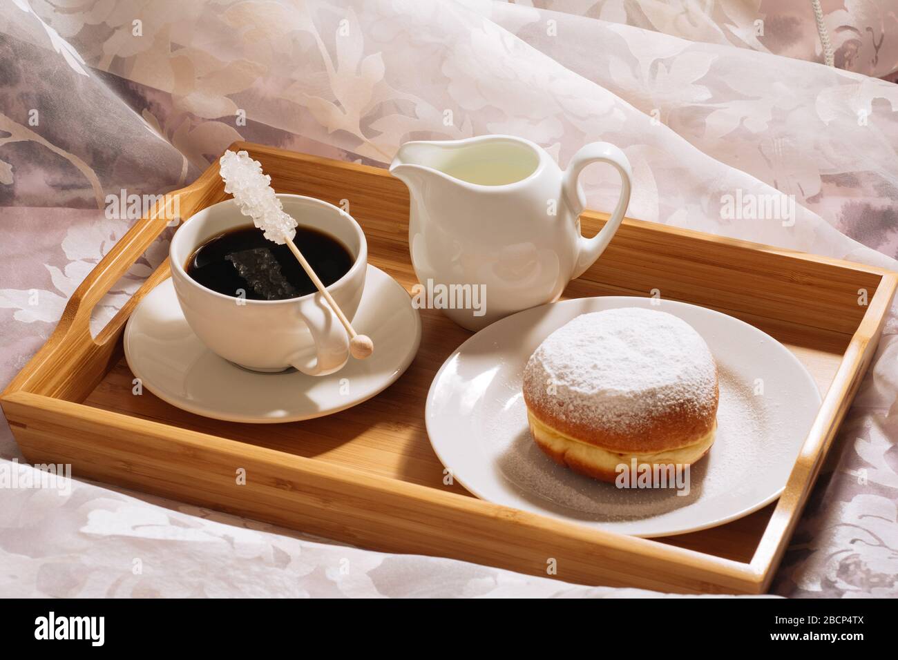 Frühes Frühstück in der Sonne mit köstlichem frischem Kaffee, Kristalllinienzucker, kalter Milch und Donut-Puderzucker auf einem Holztablett in weißen Gerichten Stockfoto