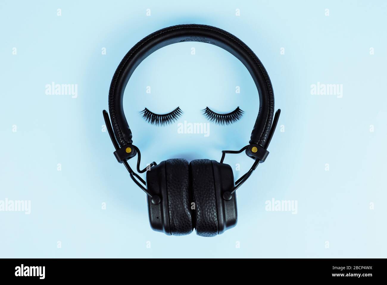 Das Konzept der Musik. Wimpelverlängerungskonzept. Bluetooth-Kopfhörer mit falschen Wimpern auf blauem Pastellhintergrund. Stockfoto