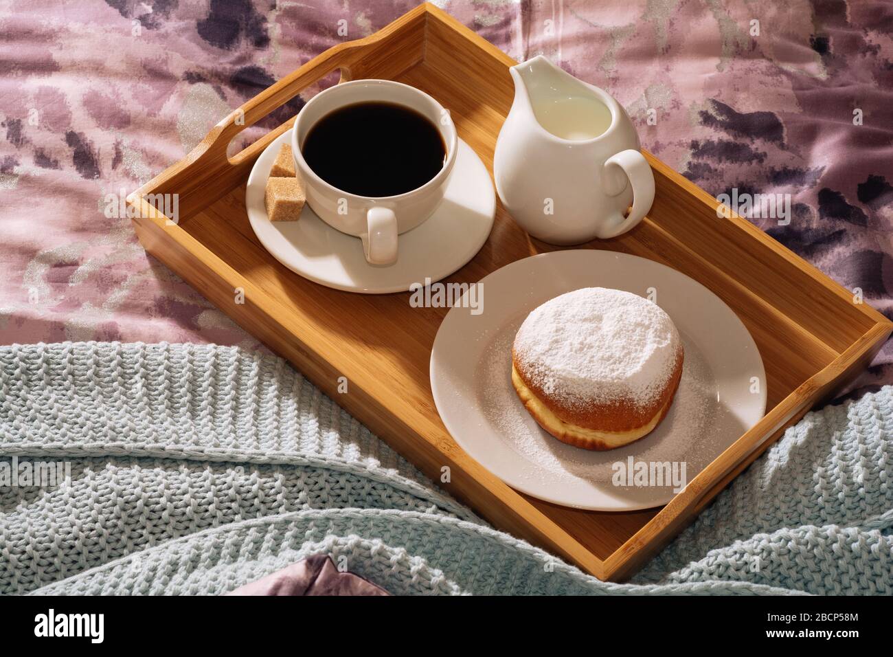 Frühstück in einem gemütlichen Bett mit frisch gebrühtem, schmackhaftem und duftendem Kaffee, Rohrzucker, frischer Milch und leckeren Donut in Puderzucker gegen ein Stockfoto