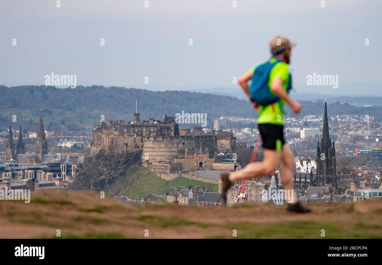 Edinburgh, Schottland, Großbritannien. April 2020. Am zweiten Sonntag des Coronavirus Sperrens in Großbritannien nimmt die Öffentlichkeit ihre tägliche Übung nicht ab. Ein Mann, der auf den Salisbury Crags im Holyrood Park mit Edinburgh Castle in der Ferne läuft. Iain Masterton/Alamy Live News Stockfoto