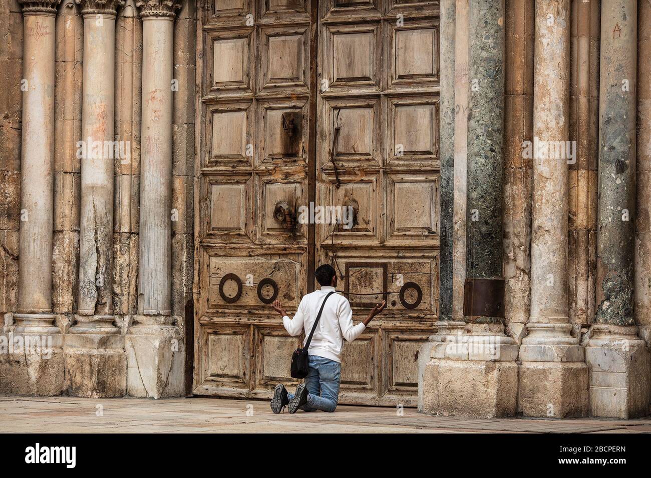 Jerusalem, Naher Osten. April 2020. Ein Mann betet während des katholischen Palmsonntags vor den verschlossenen Türen der Grabeskirche. Die Kirche befindet sich wegen des Ausbruchs von Coronavirus in einem strengen Sperrwerk. Kredit: Ilia Yefimovich / dpa / Alamy Live News Stockfoto