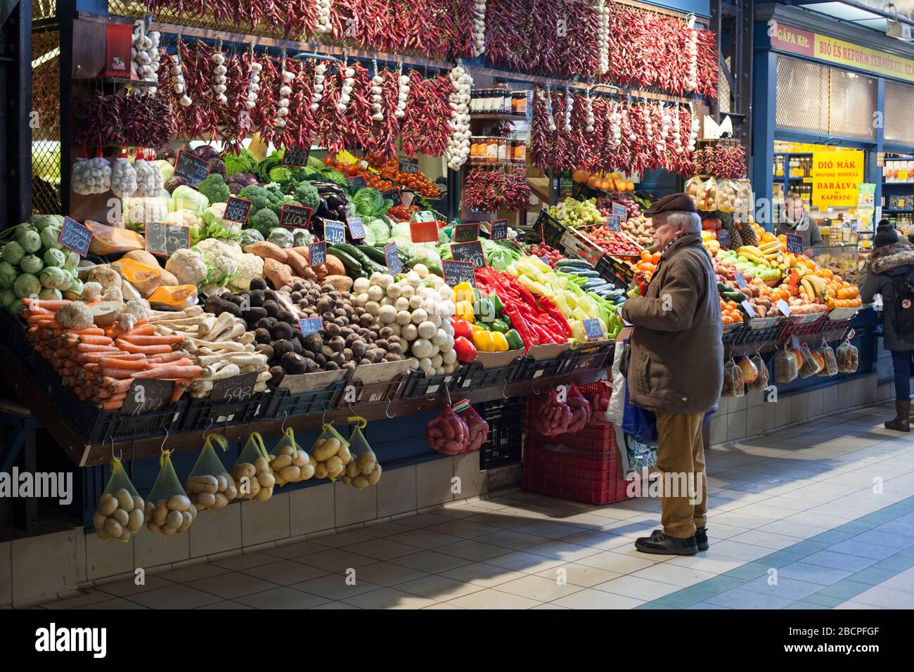 Ein Mann schaut sich im Winter auf einem Marktstand für frisches Gemüse in der Central Market Hall, Budapest, Ungarn, Produkte an Stockfoto