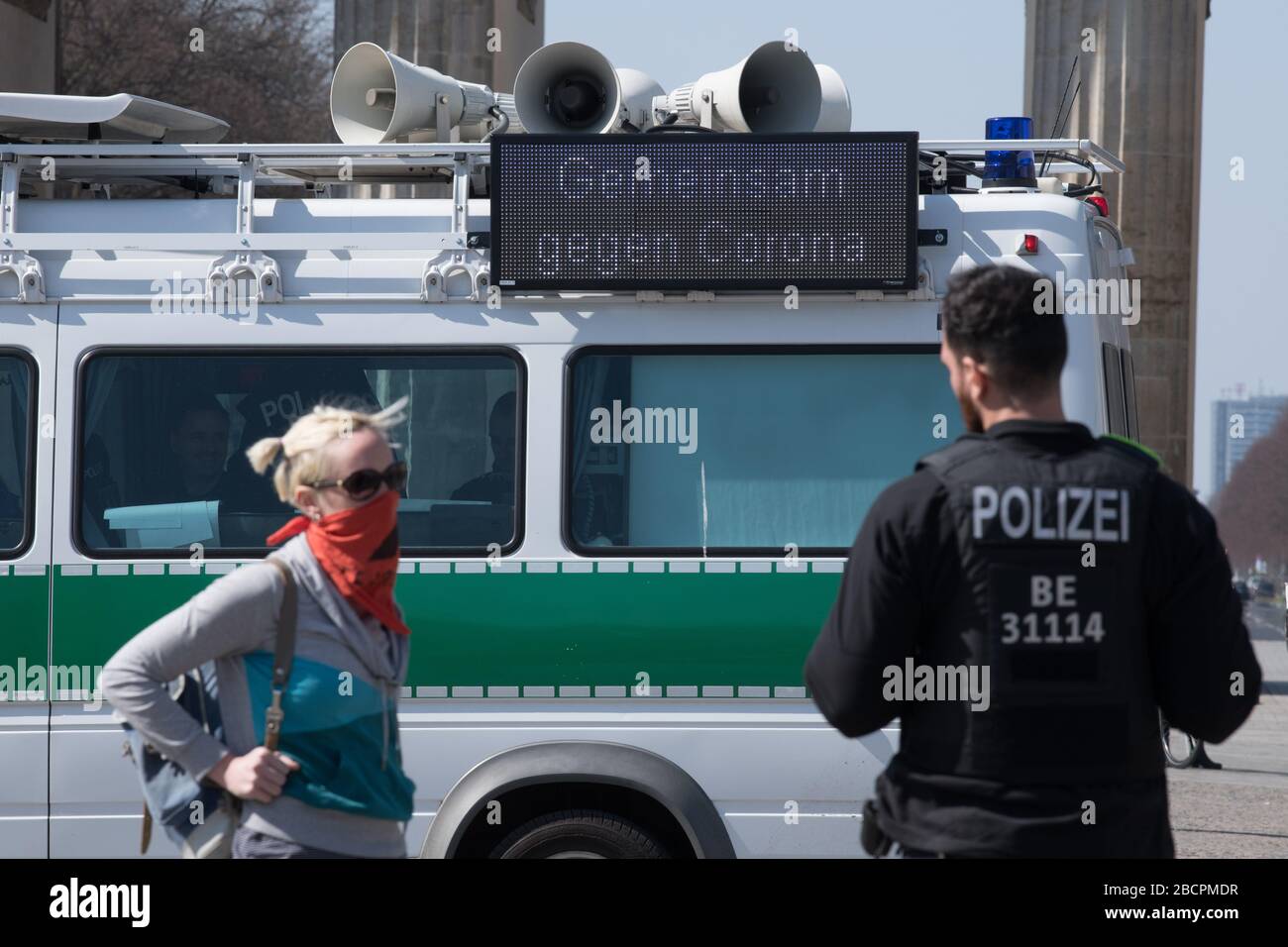 Berlin, Deutschland. April 2020. Die Formulierung "gemeinsam gegen Corona" ist auf einem Polizeifahrzeug zu sehen. Davor hört eine junge Frau mit einem in Nase und Mund gefesselten Schal einen Polizisten. Die Polizei war an verschiedenen Orten unterwegs, um zu überprüfen, ob die Vorschriften zur Eindämmung des Corona-Virus eingehalten wurden. Kredit: Jörg Carstensen / dpa / Alamy Live News Stockfoto