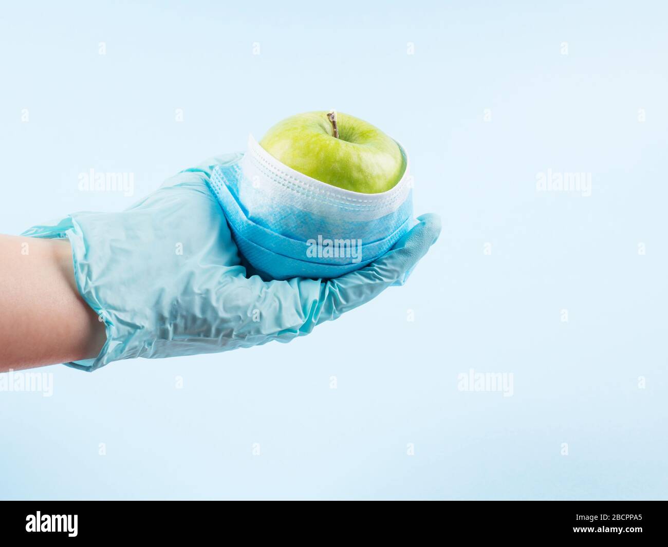 Grüner frischer apfel in Gesichtsmaske in der Hand mit Handschuh Stockfoto