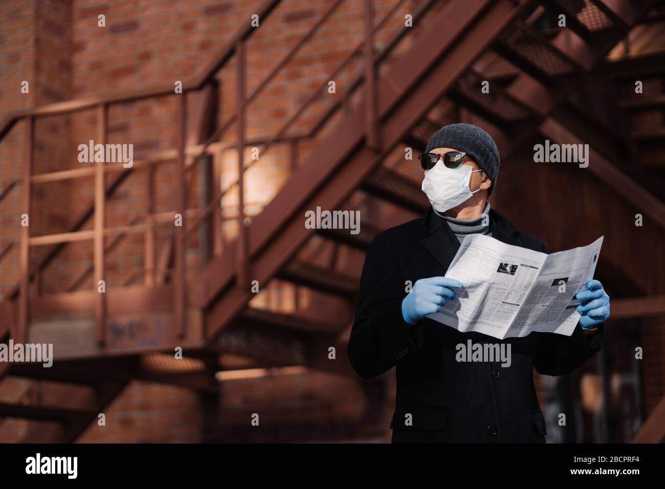 Horiontitis Schuss nachdenklichen Mann posiert mit Zeitung, trägt Schutzmaske und Gummihandschuhe, sieht beiseite, denkt über Selbstisolierung, Quarantäne und Stockfoto
